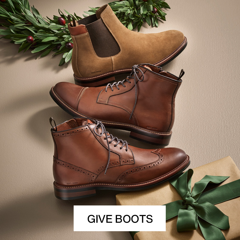 Three brown men's boots with holidcay decor surrounding them on a neutral colored background