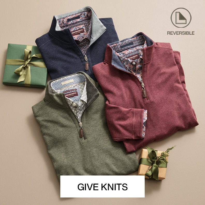 A flatlay of three folded men's quarter-zips in colors navy, red, and green. Each has a patterened button-up shirt underneath with holiday decor surrounding them on a neutral colored background.