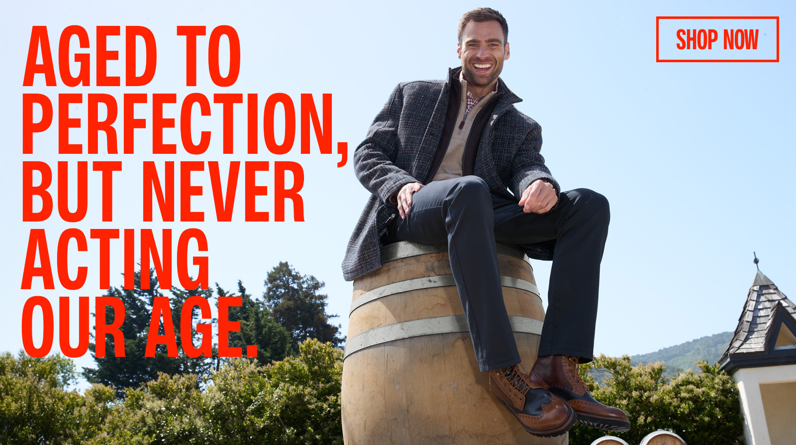 Man sitting on barrel wearing Navy coat, Navy pants, and brown and blue lace-up boots.